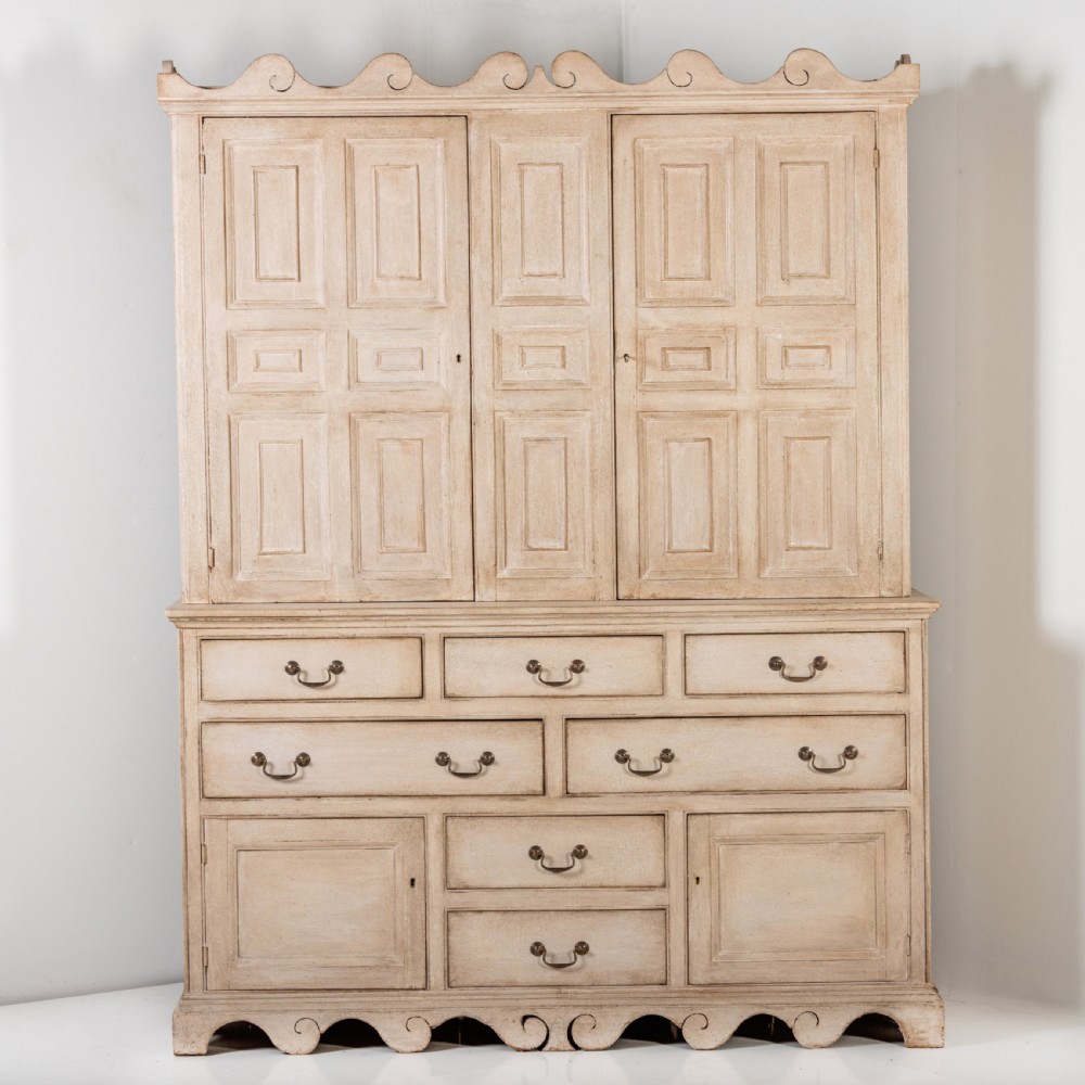A large 19th-century pale timber dresser featuring a scalloped cornice, panelled upper cupboard doors, and multiple drawers with brass drop handles above a scalloped base. View VI