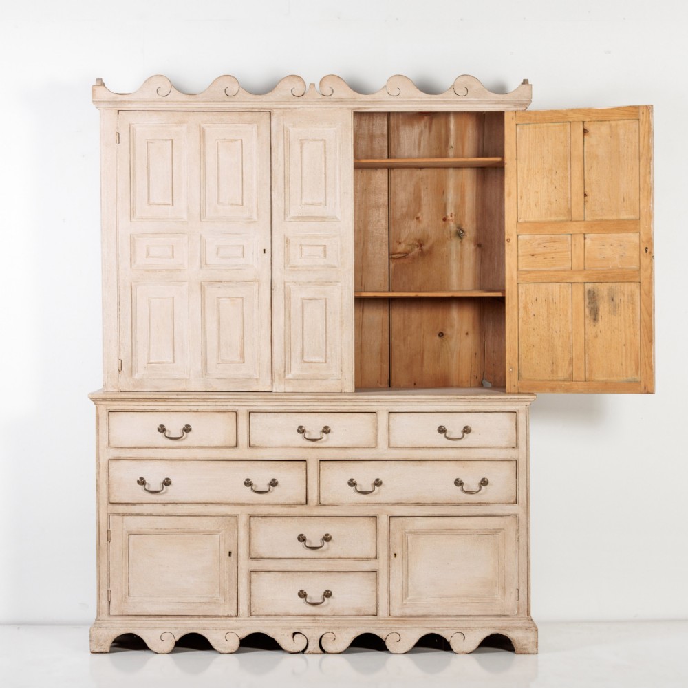 A large 19th-century pale timber dresser featuring a scalloped cornice, panelled upper cupboard doors, and multiple drawers with brass drop handles above a scalloped base. View IX
