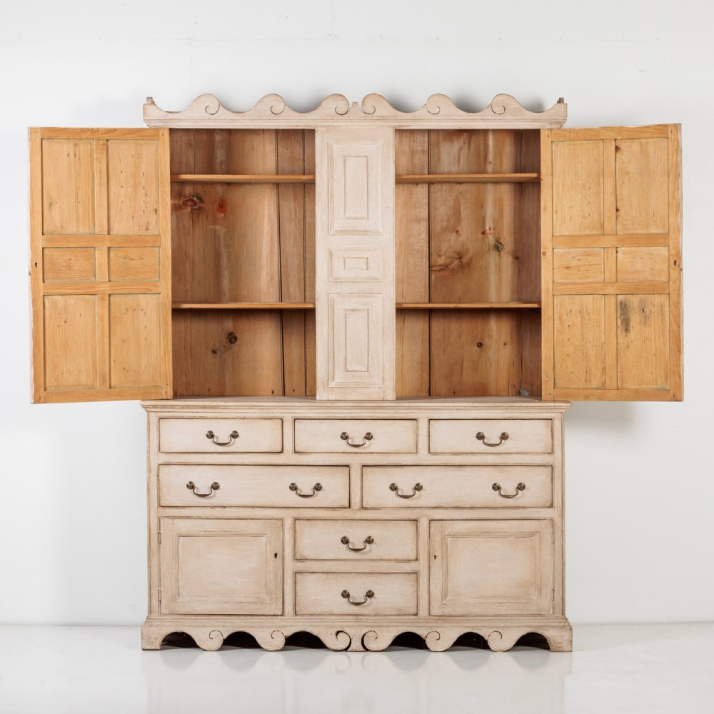 A large 19th-century pale timber dresser featuring a scalloped cornice, panelled upper cupboard doors, and multiple drawers with brass drop handles above a scalloped base. View X