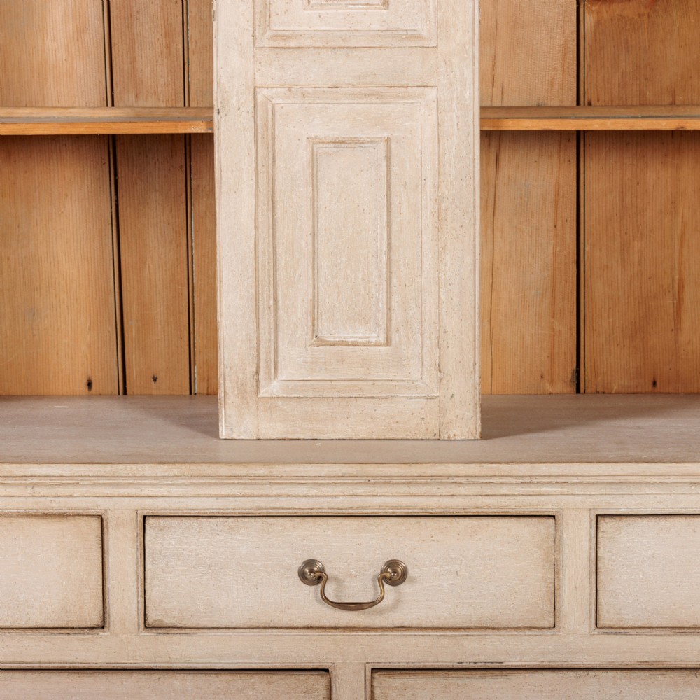 A large 19th-century pale timber dresser featuring a scalloped cornice, panelled upper cupboard doors, and multiple drawers with brass drop handles above a scalloped base. View XI