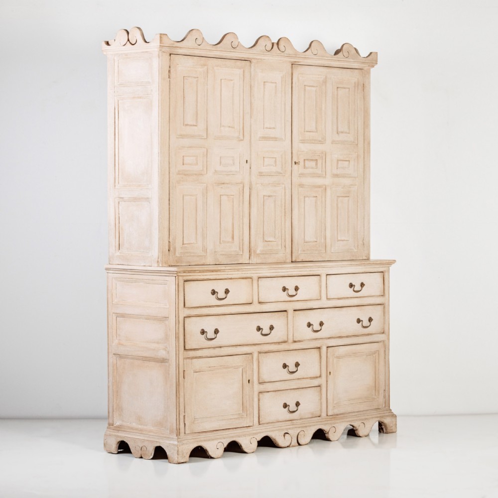 A large 19th-century pale timber dresser featuring a scalloped cornice, panelled upper cupboard doors, and multiple drawers with brass drop handles above a scalloped base. View XII