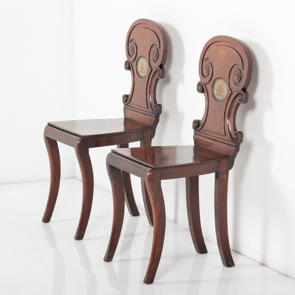 A pair of 19th-century dark mahogany hall chairs featuring scroll-carved backrests with central circular medallions and curved front legs.