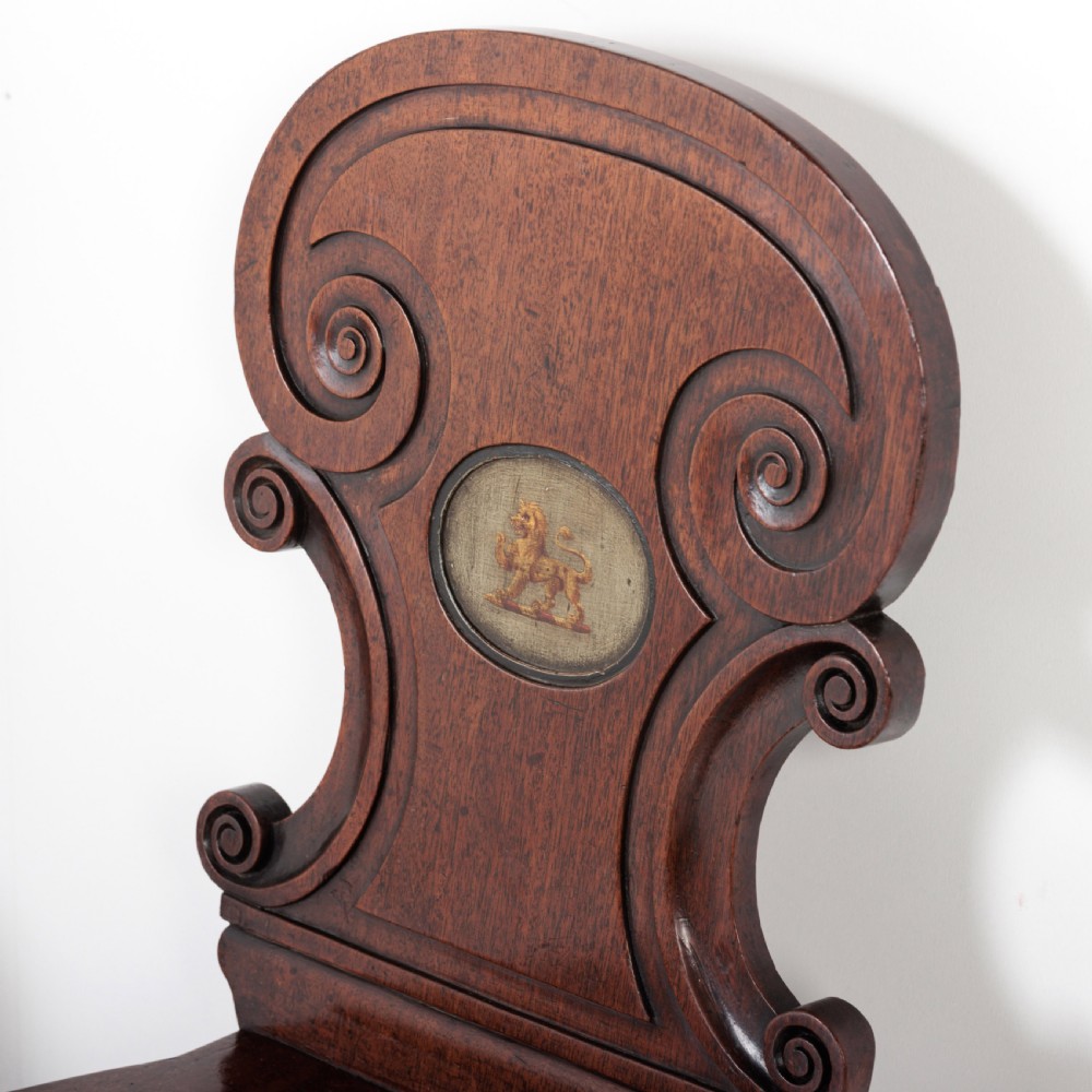 A pair of 19th-century dark mahogany hall chairs featuring scroll-carved backrests with central circular medallions and curved front legs. View II