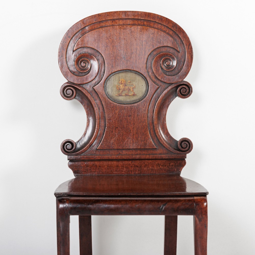 A pair of 19th-century dark mahogany hall chairs featuring scroll-carved backrests with central circular medallions and curved front legs. View VII