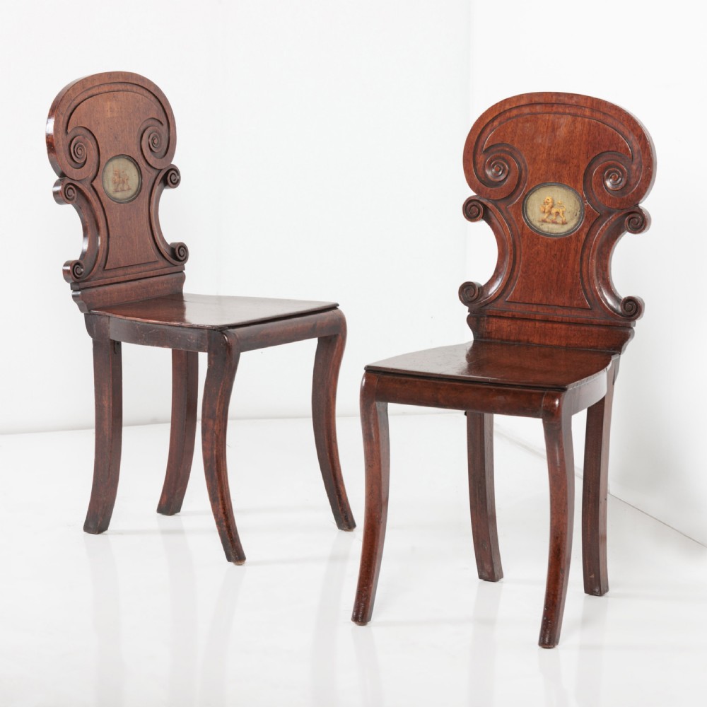 A pair of 19th-century dark mahogany hall chairs featuring scroll-carved backrests with central circular medallions and curved front legs. View IX