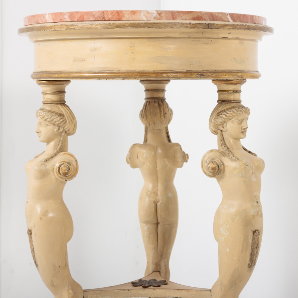 A 19th-century French Empire style circular gueridon table with a pink marble top supported by three carved cream-painted caryatid legs terminating in paw feet. View II