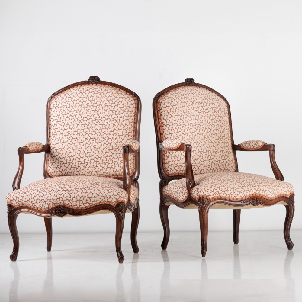 A pair of 19th-century French Louis XV style fauteuil armchairs with carved walnut frames, cabriole legs, brass stud trim, and patterned cream and brown upholstery.