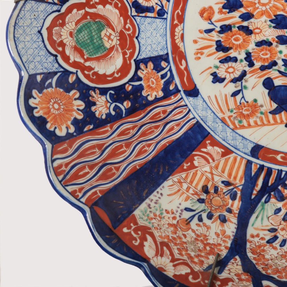 A circular Japanese Imari porcelain charger featuring a scalloped rim, hand-painted cobalt blue and rust red floral motifs, and a central vessel filled with flowers. View II