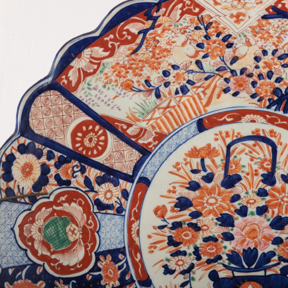 A circular Japanese Imari porcelain charger featuring a scalloped rim, hand-painted cobalt blue and rust red floral motifs, and a central vessel filled with flowers. View III