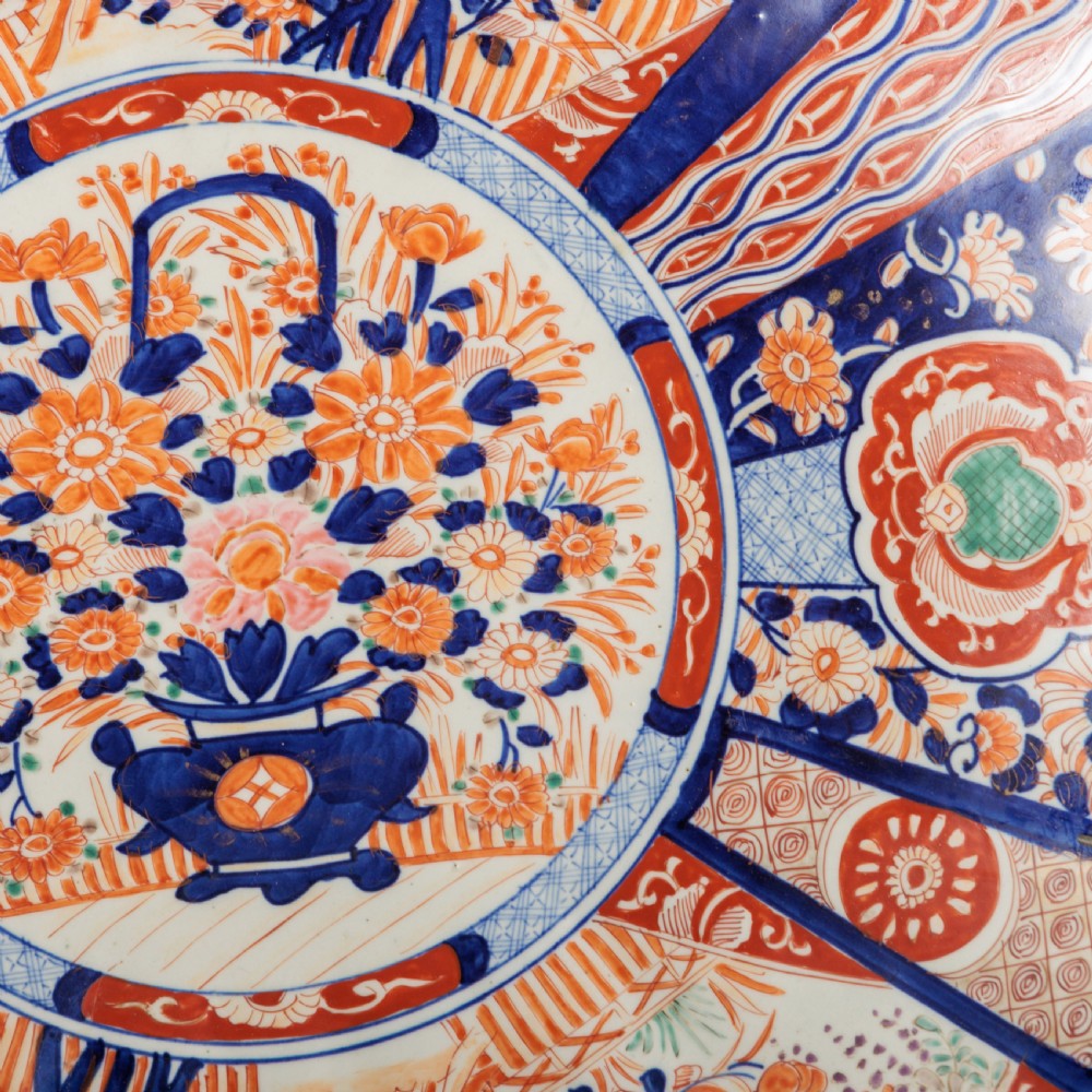 A circular Japanese Imari porcelain charger featuring a scalloped rim, hand-painted cobalt blue and rust red floral motifs, and a central vessel filled with flowers. View VI