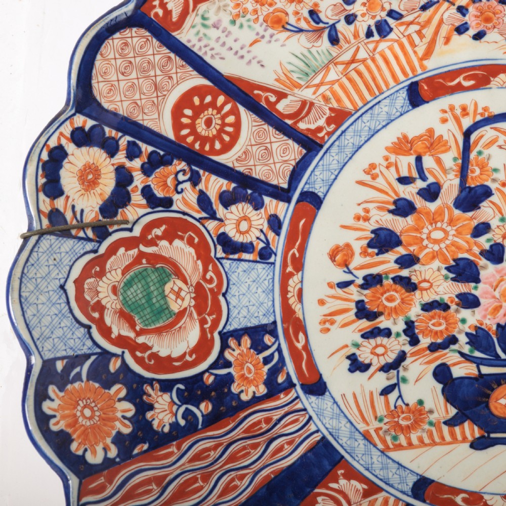 A circular Japanese Imari porcelain charger featuring a scalloped rim, hand-painted cobalt blue and rust red floral motifs, and a central vessel filled with flowers. View VII