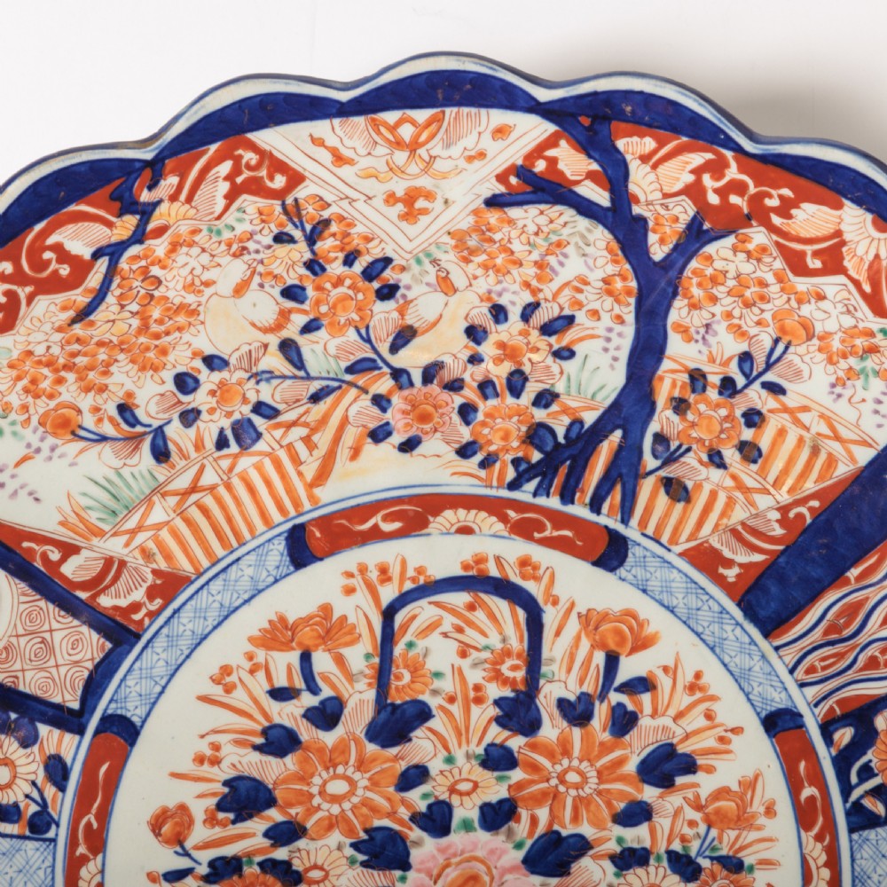 A circular Japanese Imari porcelain charger featuring a scalloped rim, hand-painted cobalt blue and rust red floral motifs, and a central vessel filled with flowers. View VIII