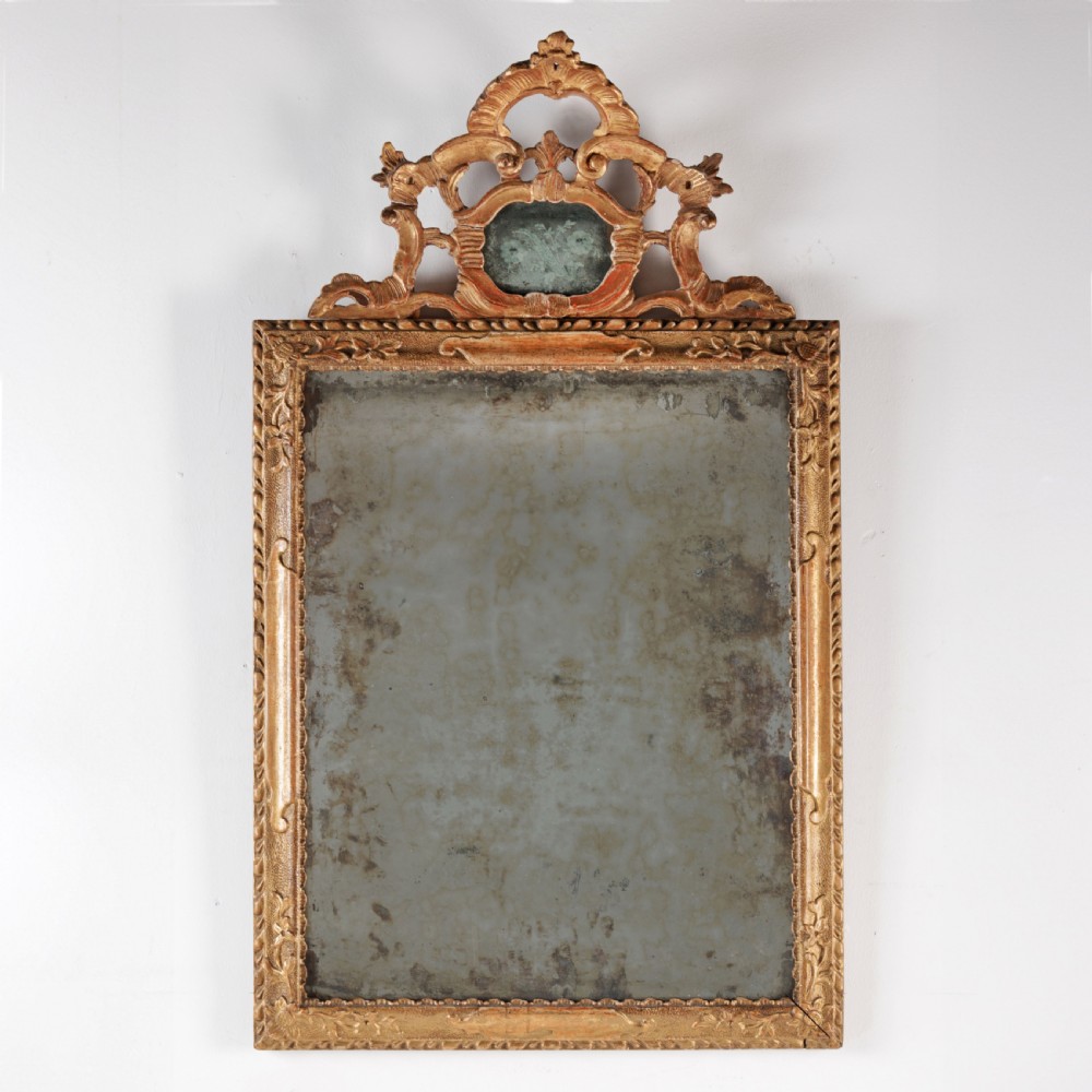 An 18th-century rectangular Venetian mirror featuring an ornate carved giltwood crest with a central cartouche and foxed mirror glass.