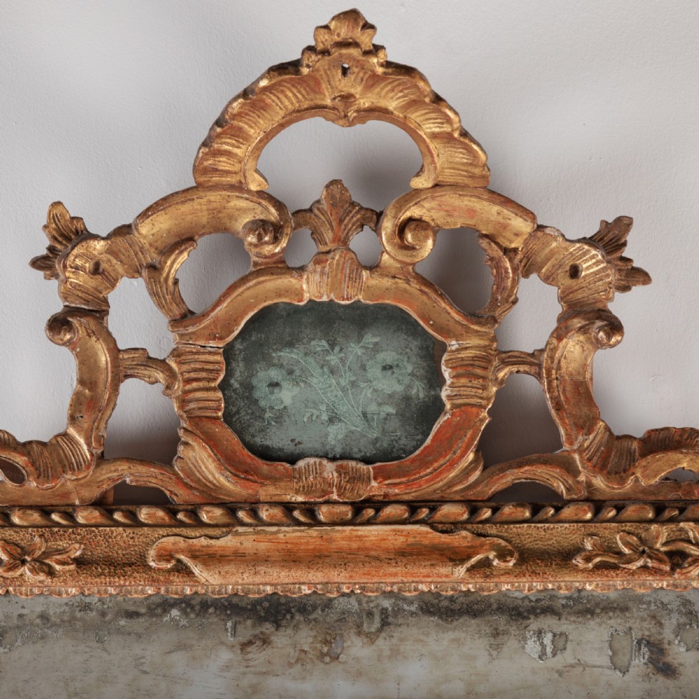 An 18th-century rectangular Venetian mirror featuring an ornate carved giltwood crest with a central cartouche and foxed mirror glass. View II