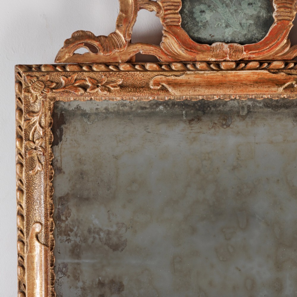 An 18th-century rectangular Venetian mirror featuring an ornate carved giltwood crest with a central cartouche and foxed mirror glass. View IV