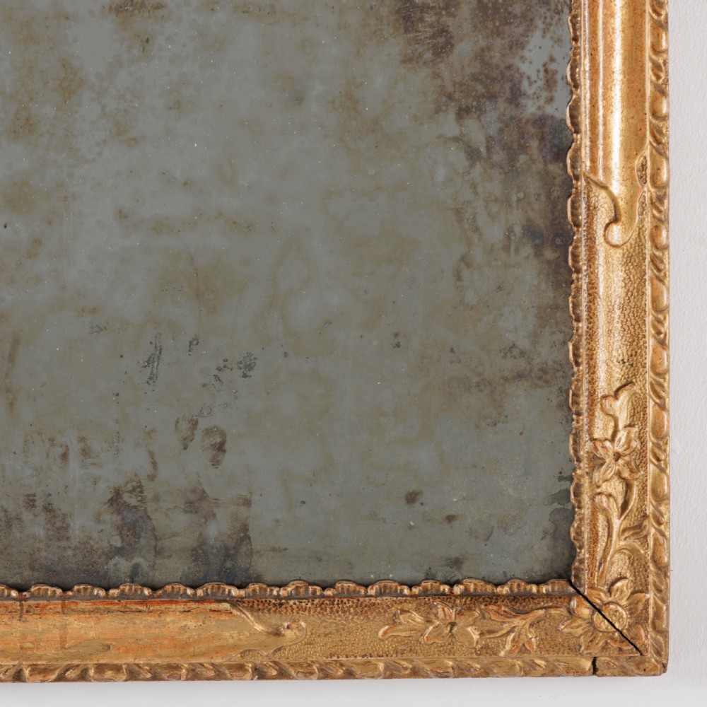 An 18th-century rectangular Venetian mirror featuring an ornate carved giltwood crest with a central cartouche and foxed mirror glass. View V