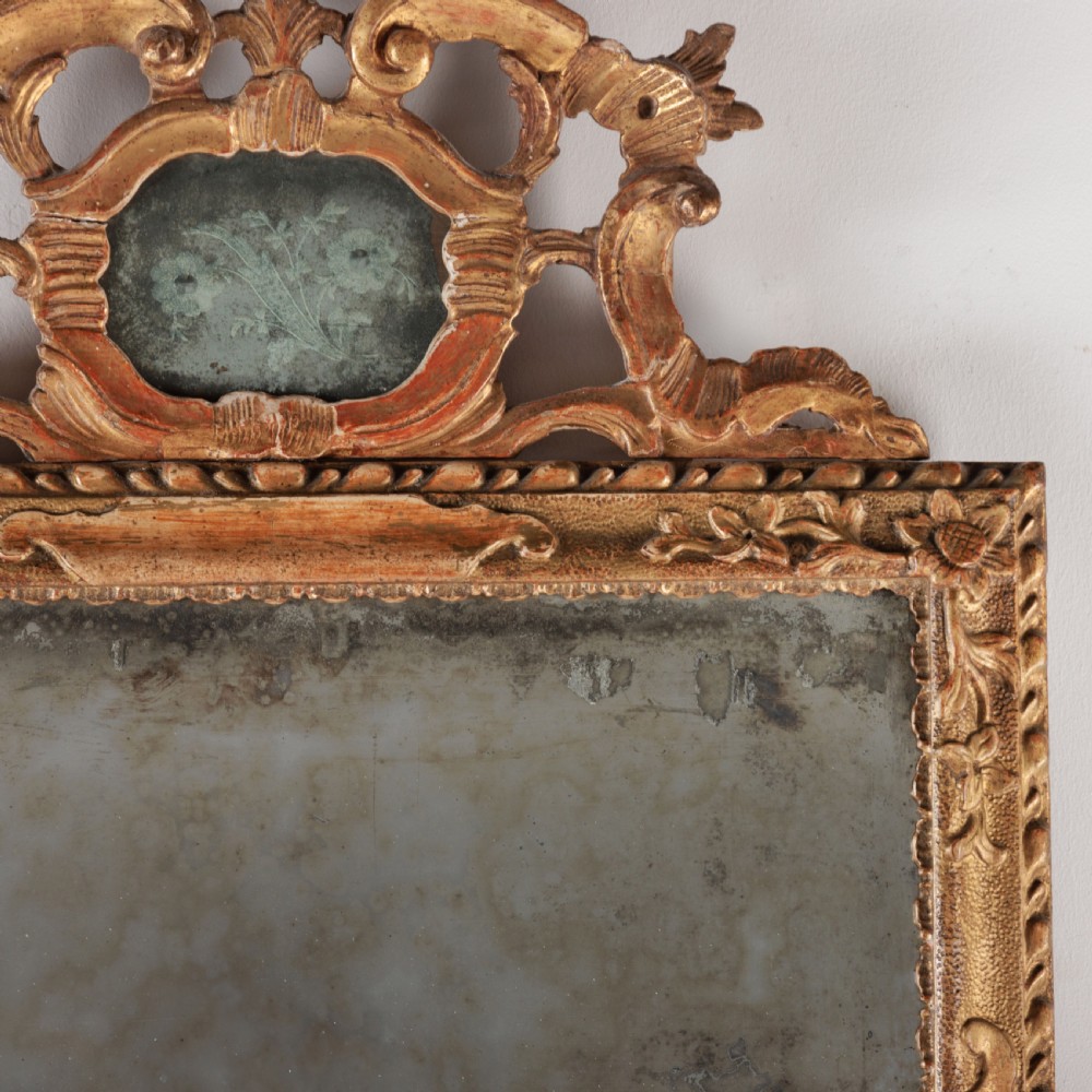 An 18th-century rectangular Venetian mirror featuring an ornate carved giltwood crest with a central cartouche and foxed mirror glass. View VI