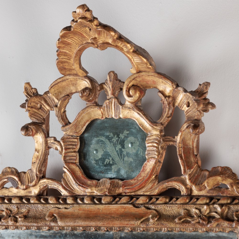 An 18th-century rectangular Venetian mirror featuring an ornate carved giltwood crest with a central cartouche and foxed mirror glass. View VII