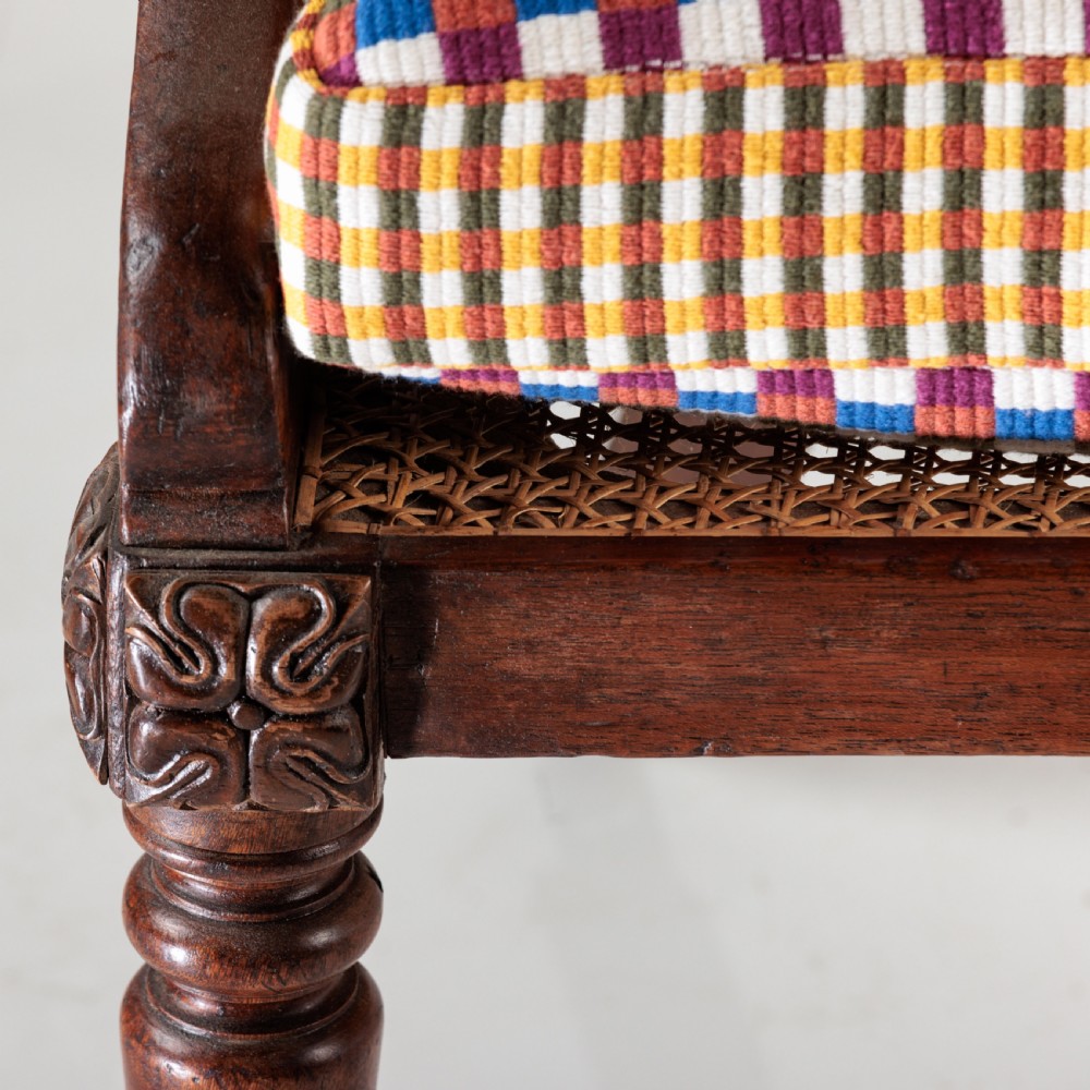 A 19th-century dark timber bergere armchair featuring woven cane back and side panels, turned front legs on brass castors, and a multi-coloured geometric patterned seat cushion. View III