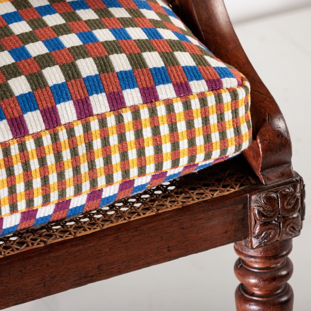 A 19th-century dark timber bergere armchair featuring woven cane back and side panels, turned front legs on brass castors, and a multi-coloured geometric patterned seat cushion. View IV