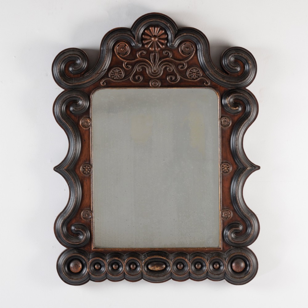 A dark brown carved wood wall mirror featuring elaborate scrollwork, rosette medallions, and a rectangular mirror glass.