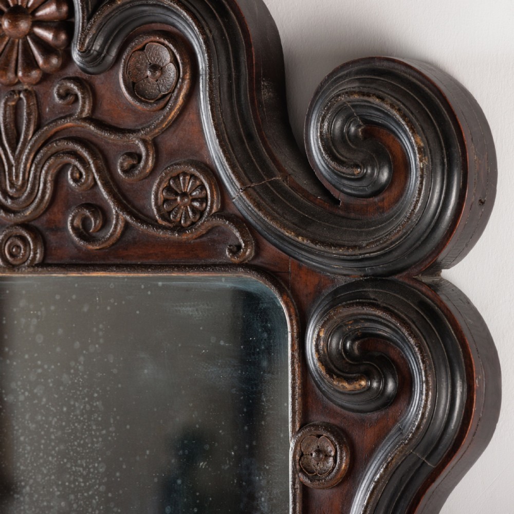 A dark brown carved wood wall mirror featuring elaborate scrollwork, rosette medallions, and a rectangular mirror glass. View VI