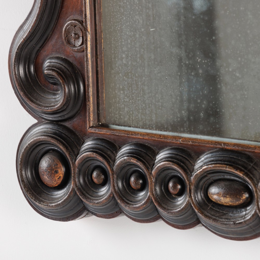A dark brown carved wood wall mirror featuring elaborate scrollwork, rosette medallions, and a rectangular mirror glass. View IX