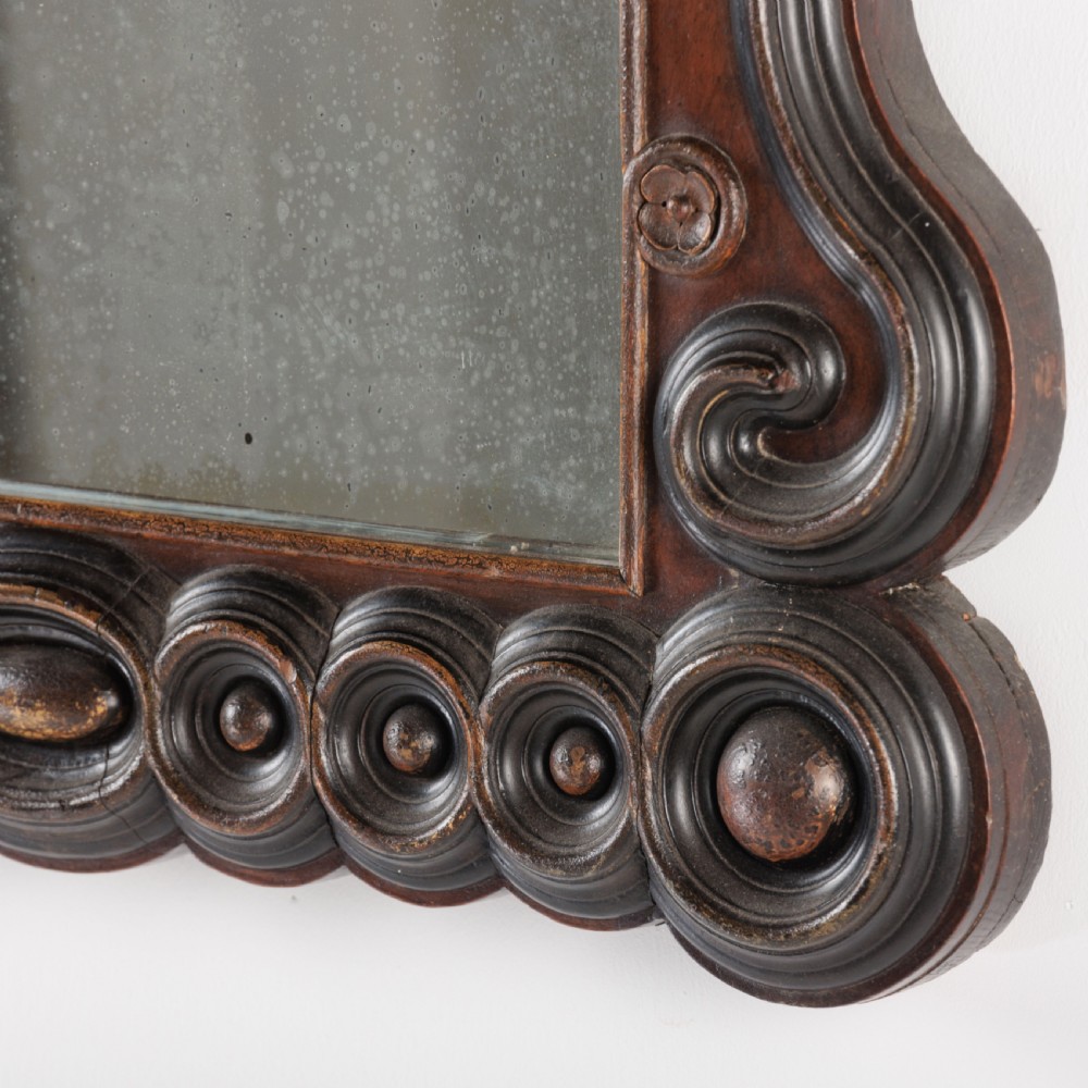 A dark brown carved wood wall mirror featuring elaborate scrollwork, rosette medallions, and a rectangular mirror glass. View X