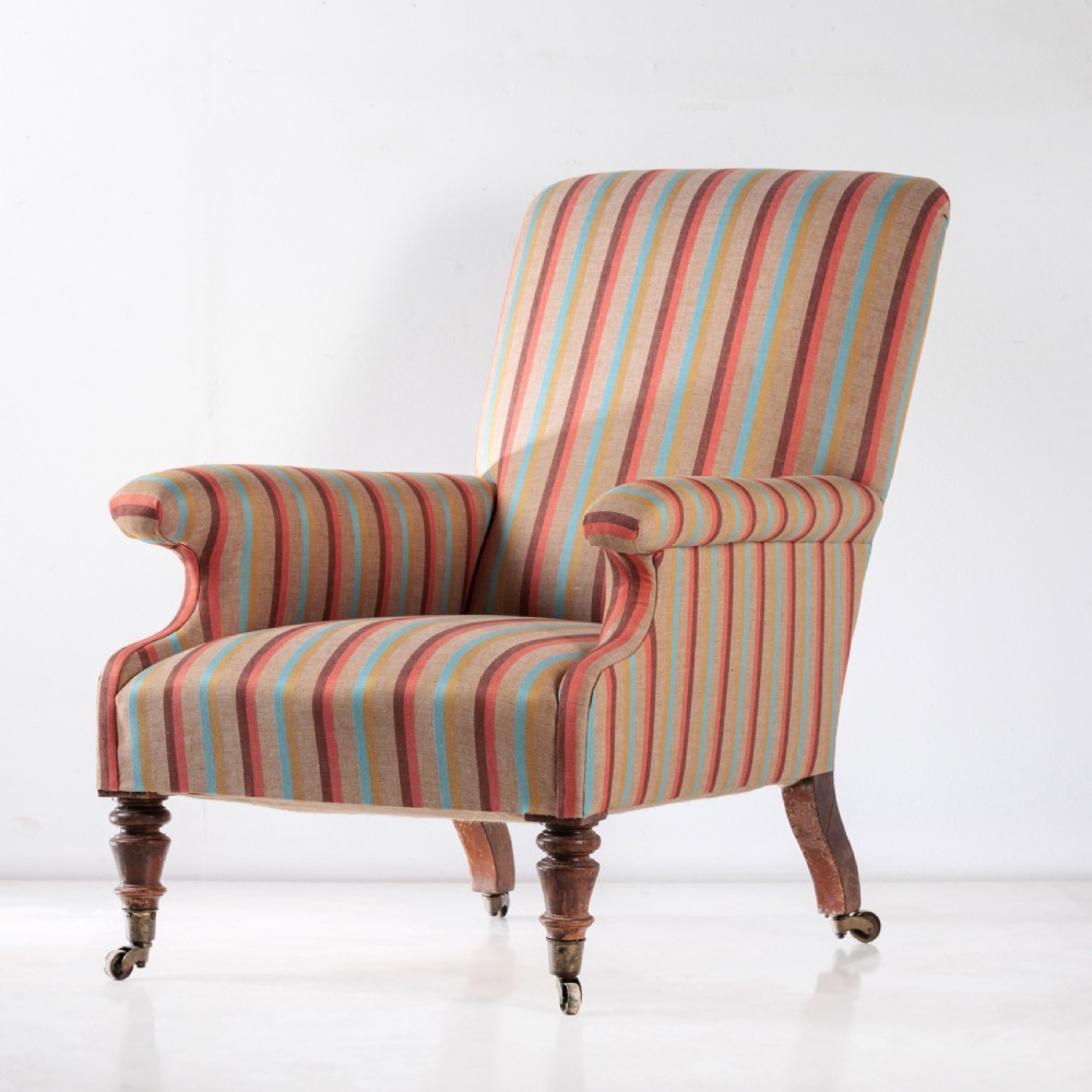 A 19th-century Victorian easy armchair upholstered in vertical stripes of terracotta, blue, beige, and gold with turned timber front legs on brass castors.