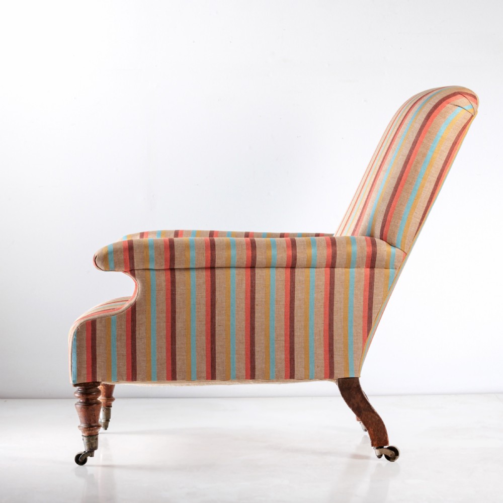A 19th-century Victorian easy armchair upholstered in vertical stripes of terracotta, blue, beige, and gold with turned timber front legs on brass castors. View V