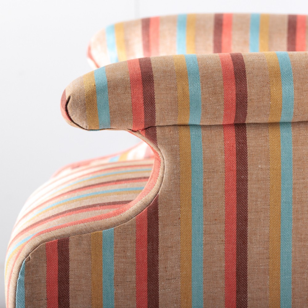 A 19th-century Victorian easy armchair upholstered in vertical stripes of terracotta, blue, beige, and gold with turned timber front legs on brass castors. View X