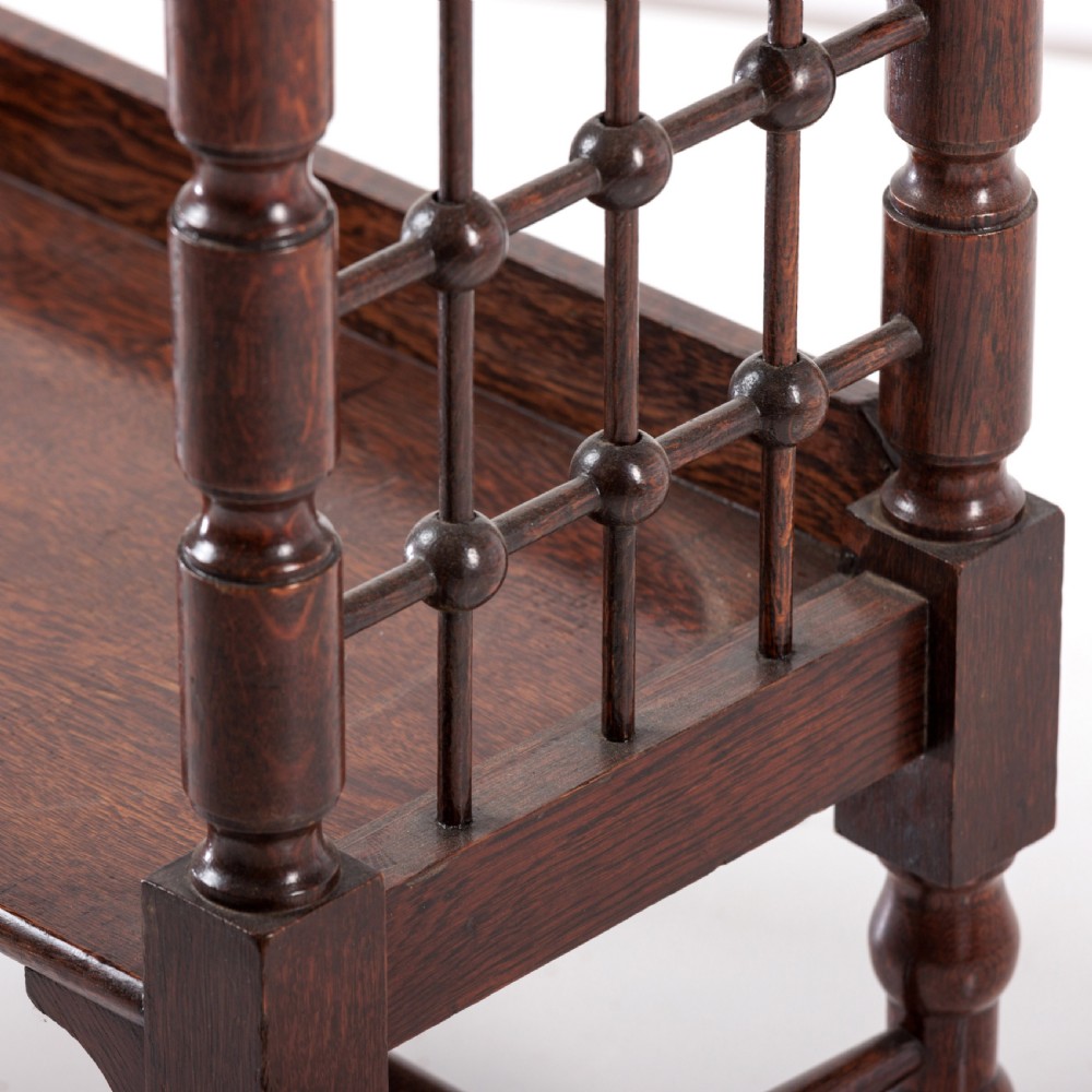 A dark oak Aesthetic Movement side table featuring turned spindle supports, side spindle galleries, three tiers, and legs terminating in castors. View III