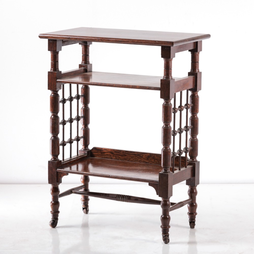 A dark oak Aesthetic Movement side table featuring turned spindle supports, side spindle galleries, three tiers, and legs terminating in castors. View IV
