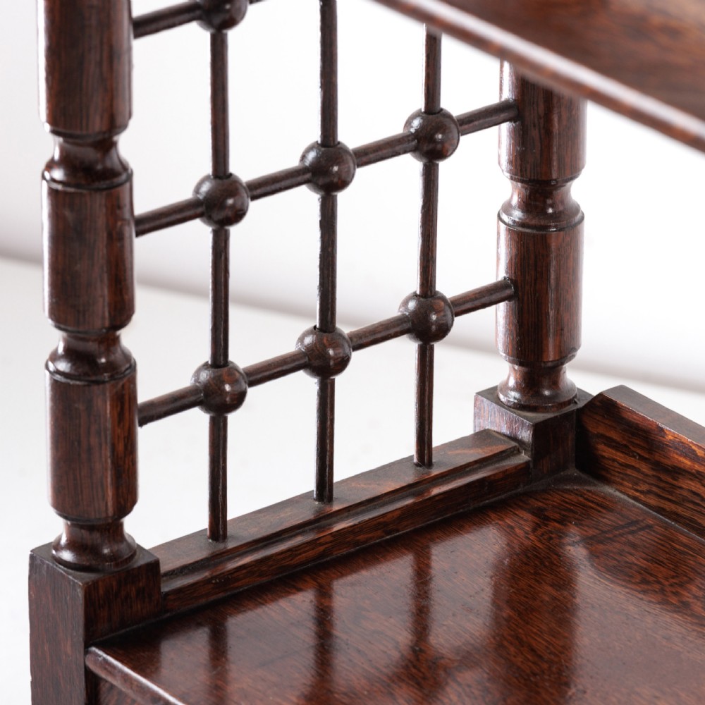 A dark oak Aesthetic Movement side table featuring turned spindle supports, side spindle galleries, three tiers, and legs terminating in castors. View V