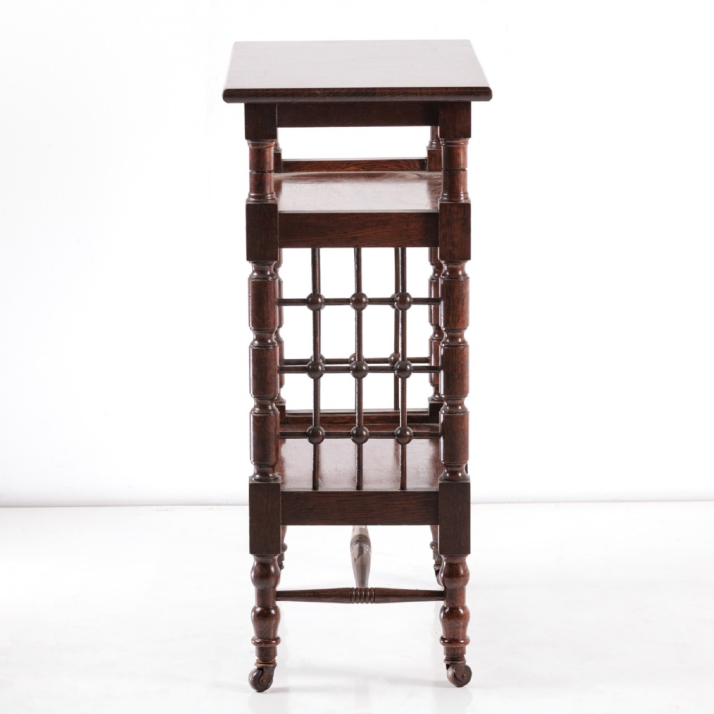 A dark oak Aesthetic Movement side table featuring turned spindle supports, side spindle galleries, three tiers, and legs terminating in castors. View VI