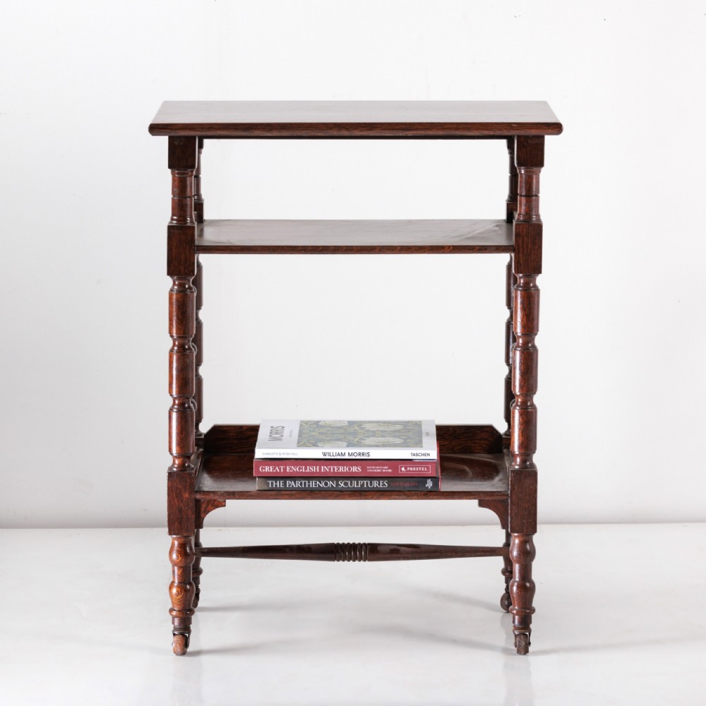 A dark oak Aesthetic Movement side table featuring turned spindle supports, side spindle galleries, three tiers, and legs terminating in castors. View VII