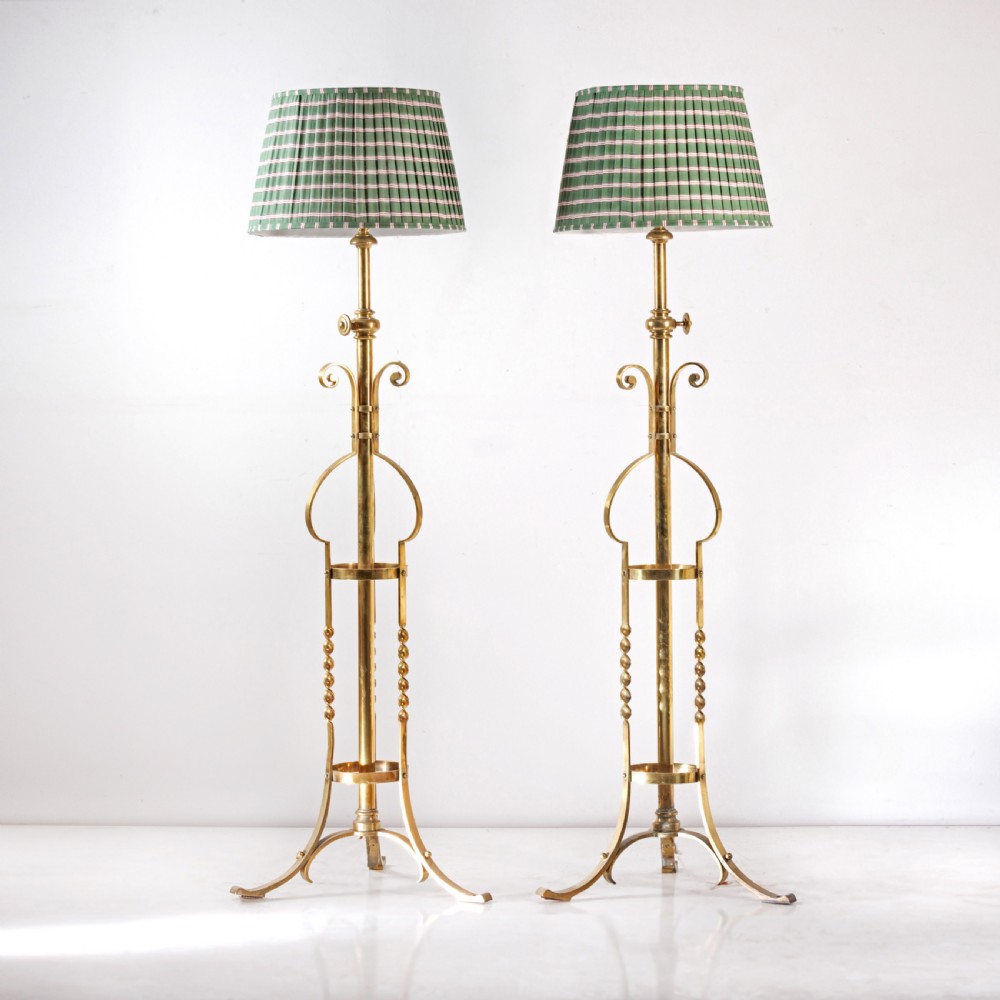 A pair of antique brass standard floor lamps featuring tripod bases, scrolled design details, and green striped pleated fabric shades.