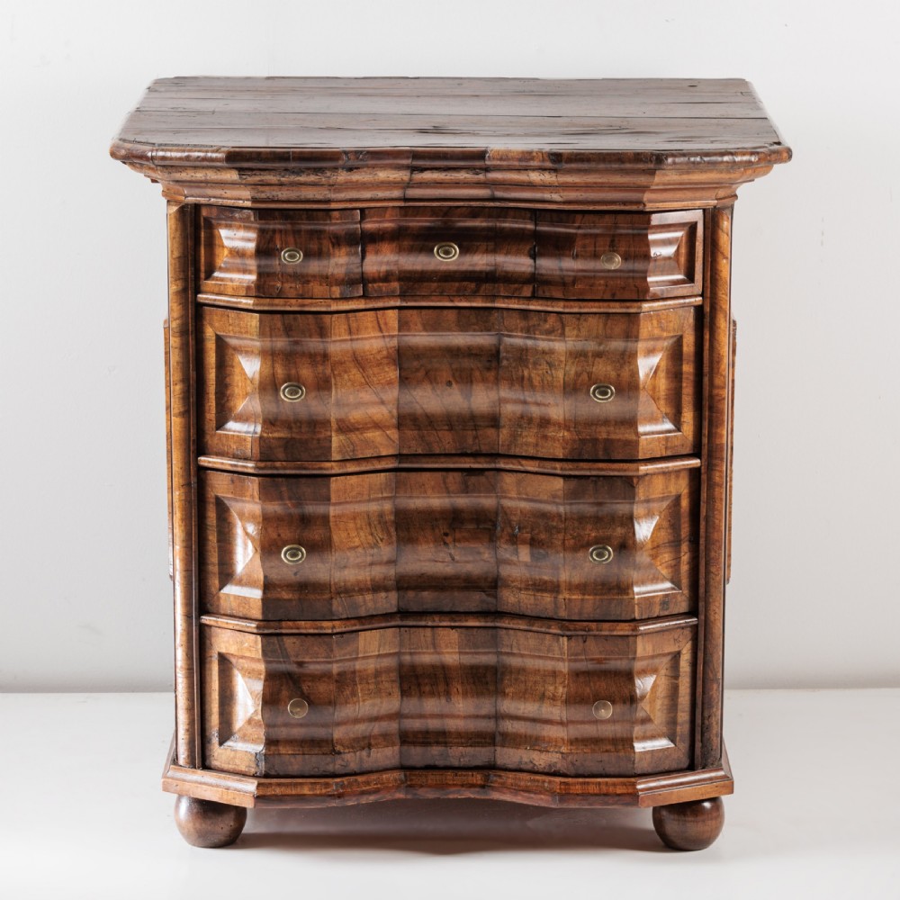 An 18th-century Bavarian walnut chest of drawers featuring a serpentine front, four moulded drawers with brass knobs, panelled sides, and turned bun feet. View II