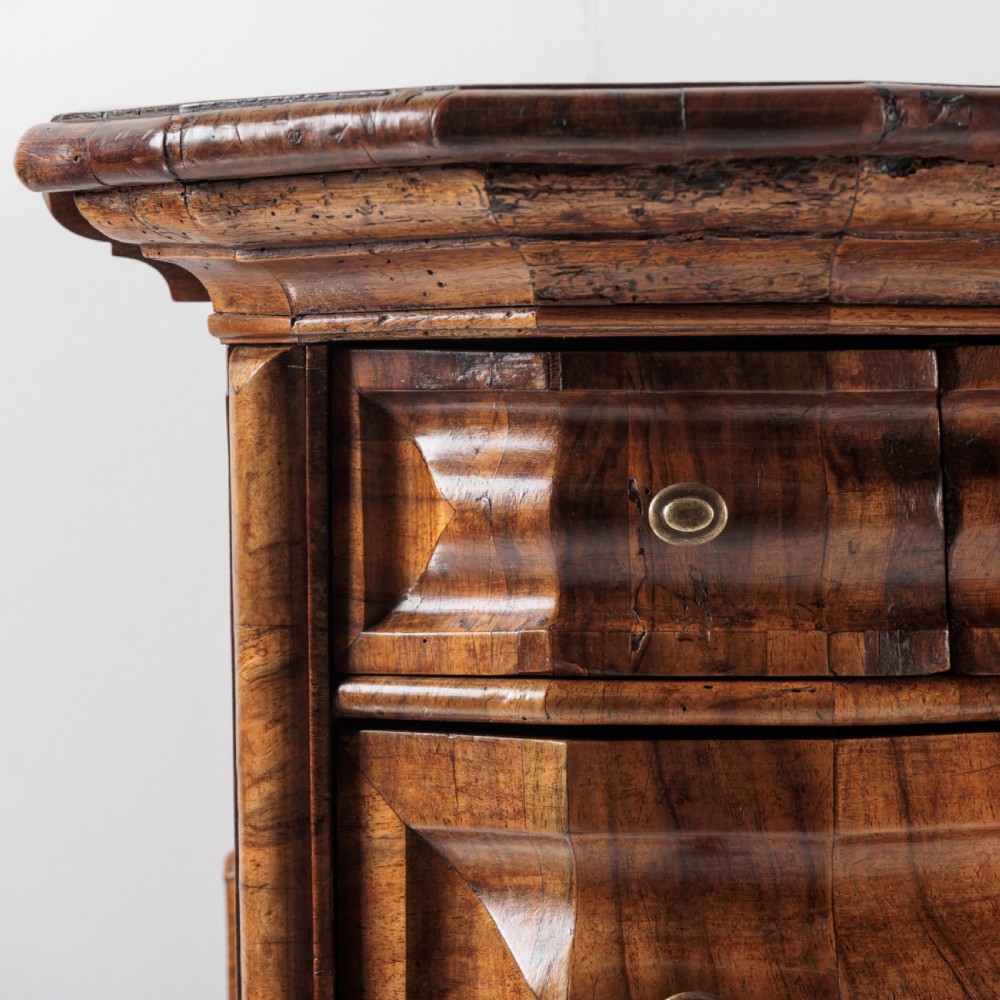 An 18th-century Bavarian walnut chest of drawers featuring a serpentine front, four moulded drawers with brass knobs, panelled sides, and turned bun feet. View VI