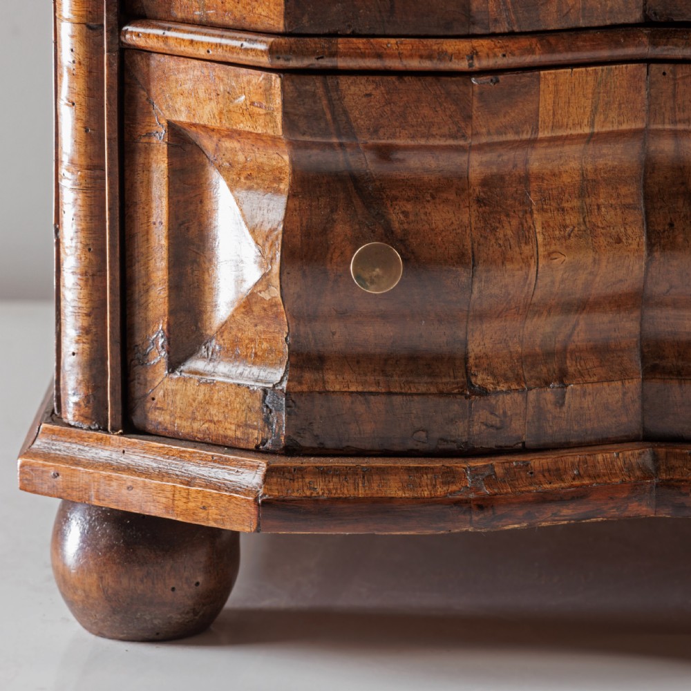 An 18th-century Bavarian walnut chest of drawers featuring a serpentine front, four moulded drawers with brass knobs, panelled sides, and turned bun feet. View IX