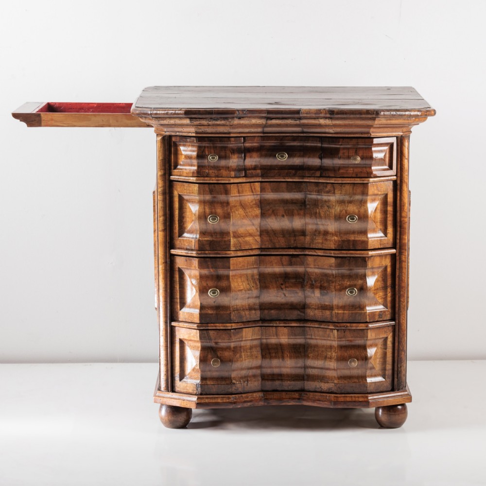 An 18th-century Bavarian walnut chest of drawers featuring a serpentine front, four moulded drawers with brass knobs, panelled sides, and turned bun feet. View X