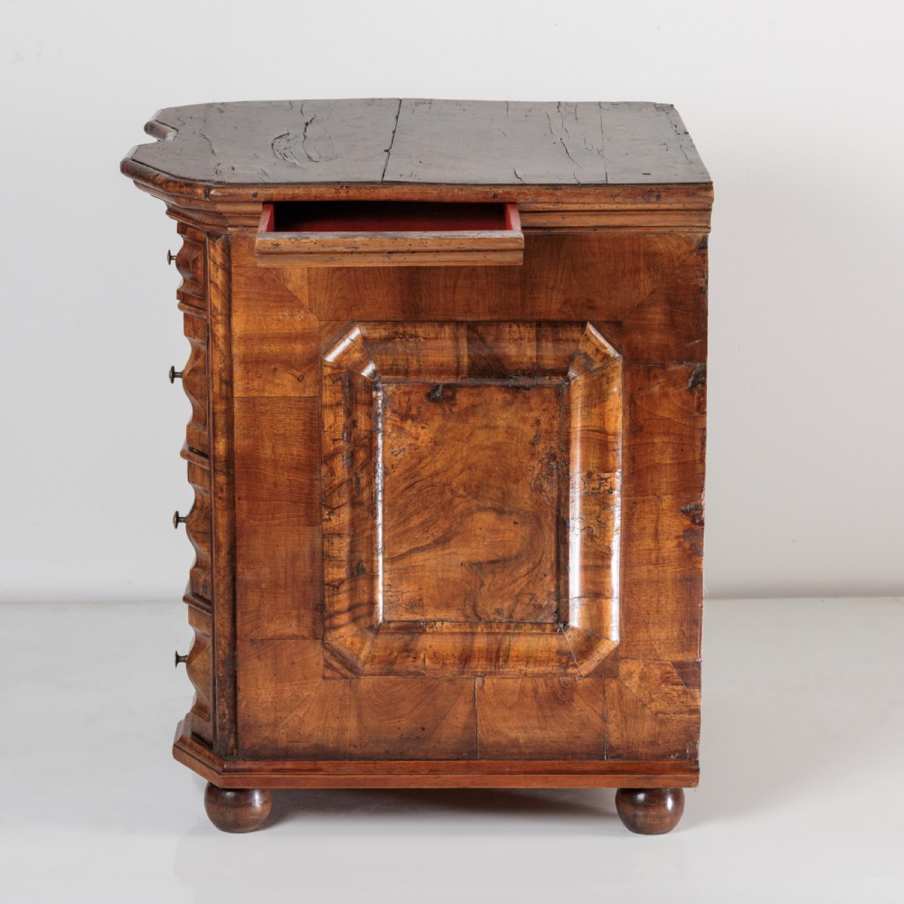 An 18th-century Bavarian walnut chest of drawers featuring a serpentine front, four moulded drawers with brass knobs, panelled sides, and turned bun feet. View XI