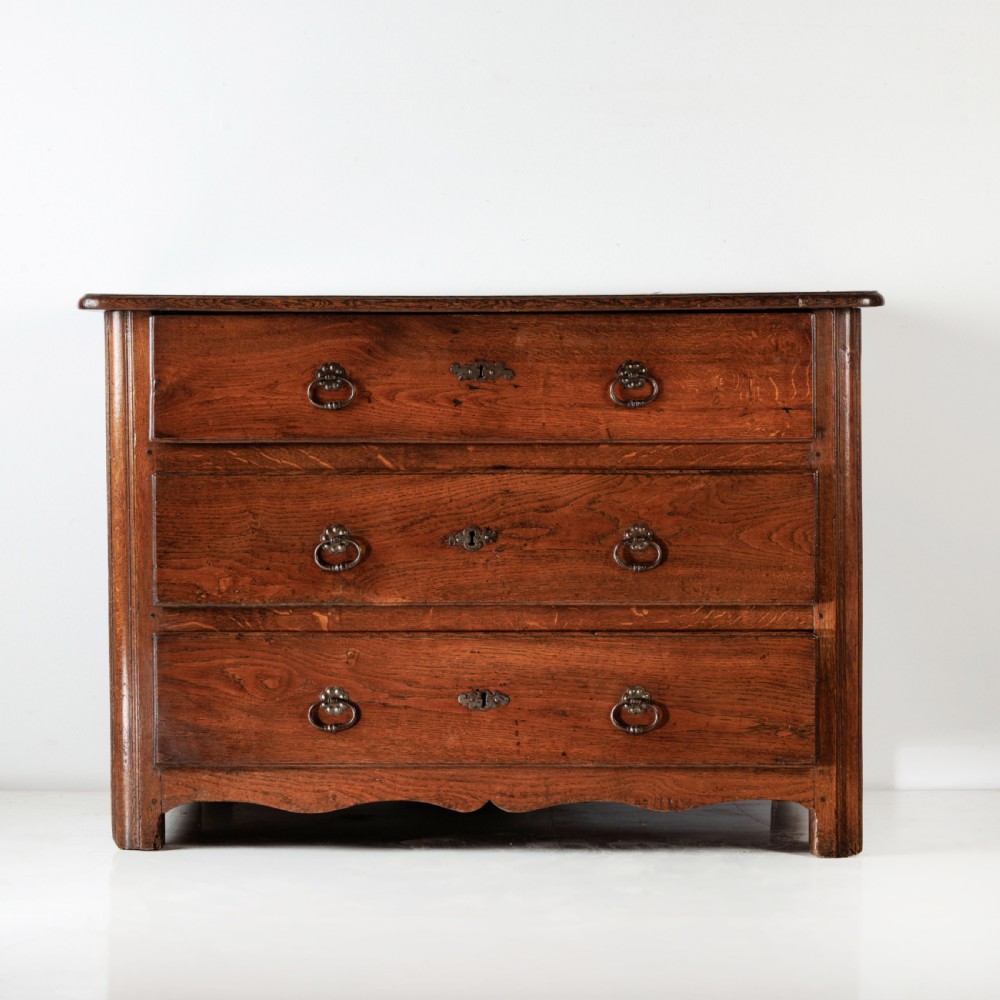 A nineteenth-century provincial oak chest of drawers with three full-width drawers featuring metal drop handles and decorative keyhole escutcheons.