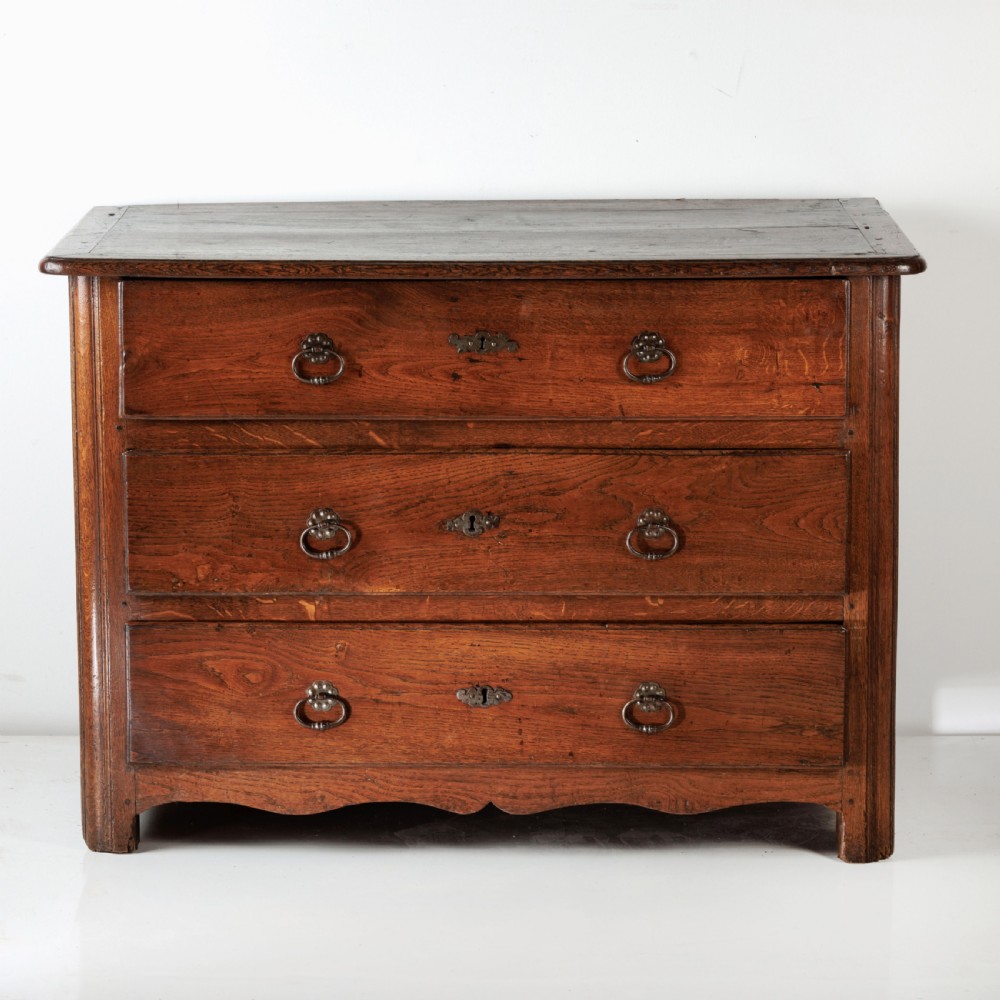 A nineteenth-century provincial oak chest of drawers with three full-width drawers featuring metal drop handles and decorative keyhole escutcheons. View II