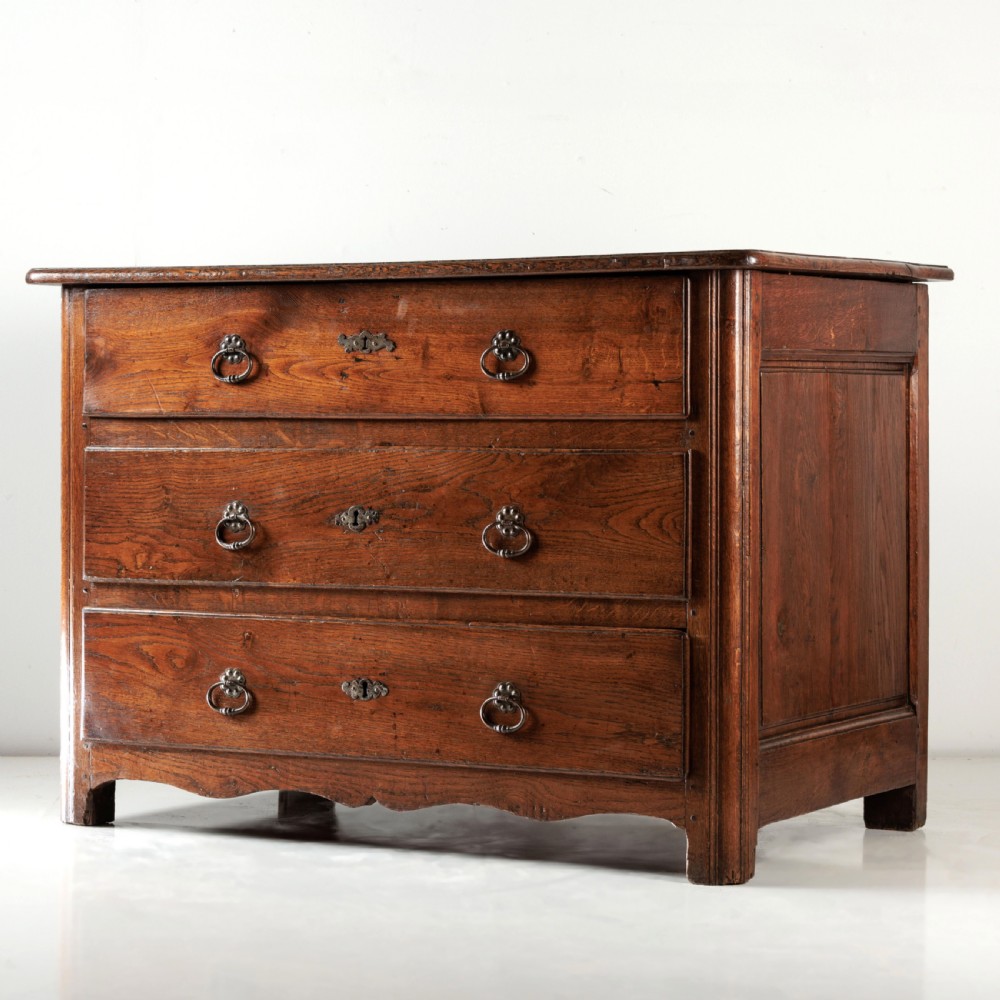 A nineteenth-century provincial oak chest of drawers with three full-width drawers featuring metal drop handles and decorative keyhole escutcheons. View V