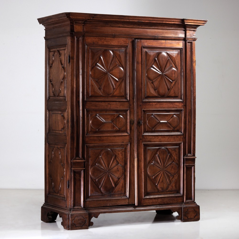 A large seventeenth-century Italian walnut cabinet featuring two tall panelled doors with carved geometric star relief motifs, framed by moulded side pilasters and resting on bracket feet.