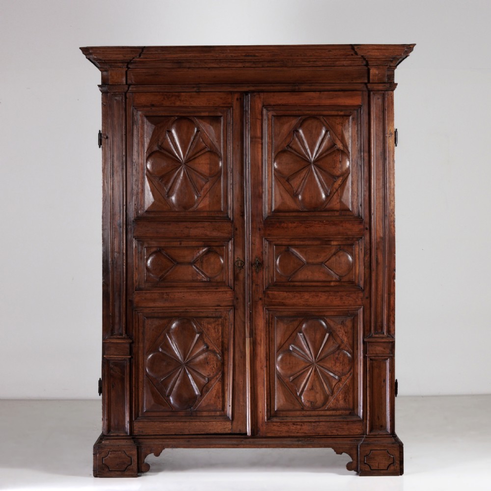 A large seventeenth-century Italian walnut cabinet featuring two tall panelled doors with carved geometric star relief motifs, framed by moulded side pilasters and resting on bracket feet. View II