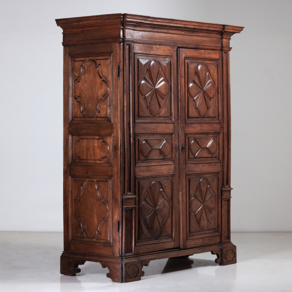 A large seventeenth-century Italian walnut cabinet featuring two tall panelled doors with carved geometric star relief motifs, framed by moulded side pilasters and resting on bracket feet. View III