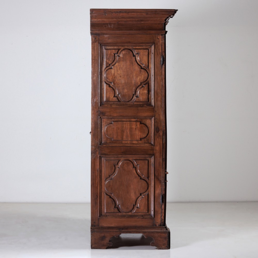 A large seventeenth-century Italian walnut cabinet featuring two tall panelled doors with carved geometric star relief motifs, framed by moulded side pilasters and resting on bracket feet. View IV