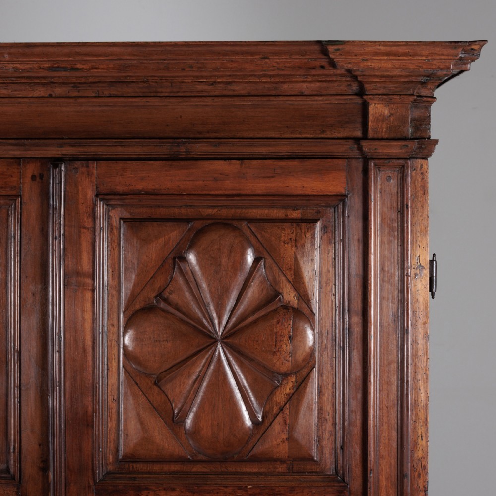 A large seventeenth-century Italian walnut cabinet featuring two tall panelled doors with carved geometric star relief motifs, framed by moulded side pilasters and resting on bracket feet. View V
